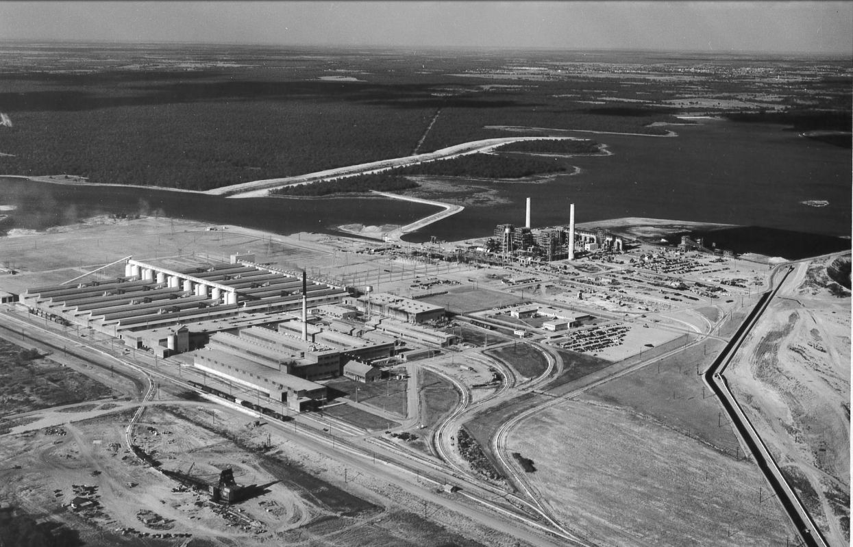 Historic aerial photo of Alcoa Rockdale Works, with long smelting buildings, rail lines, the power plant with two stacks, and the lake beyond